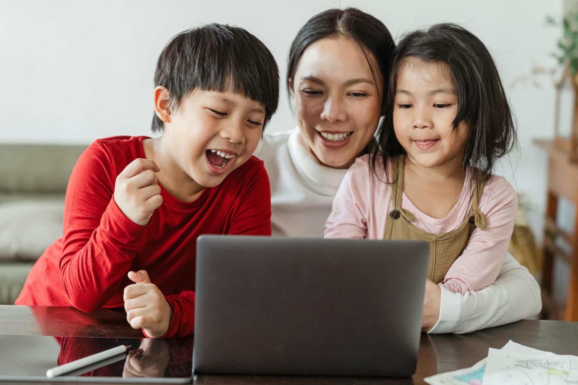 A mom and her two children are on a sofa looking at a laptop computer.