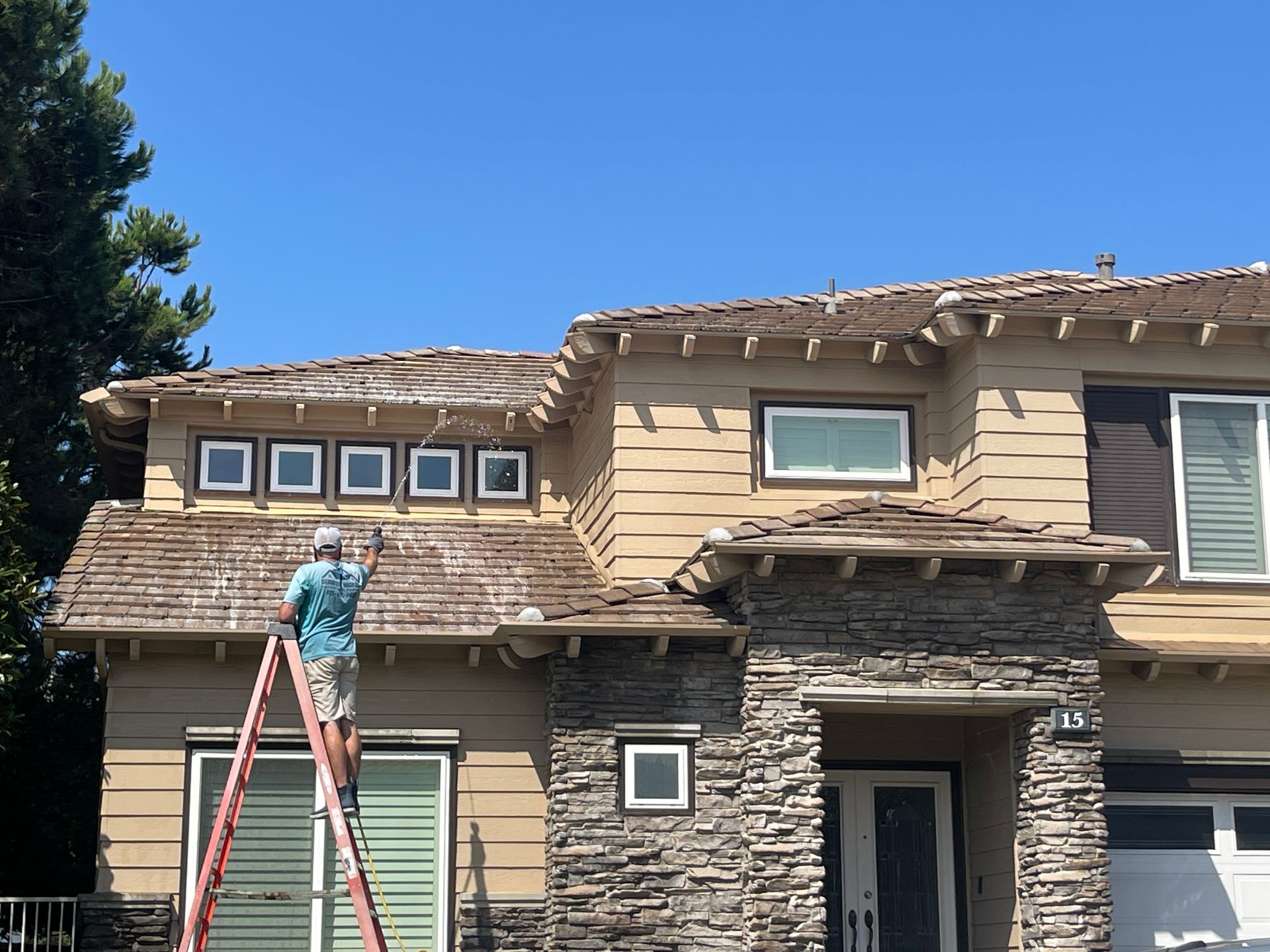 A man is standing on a ladder painting the roof of a house.