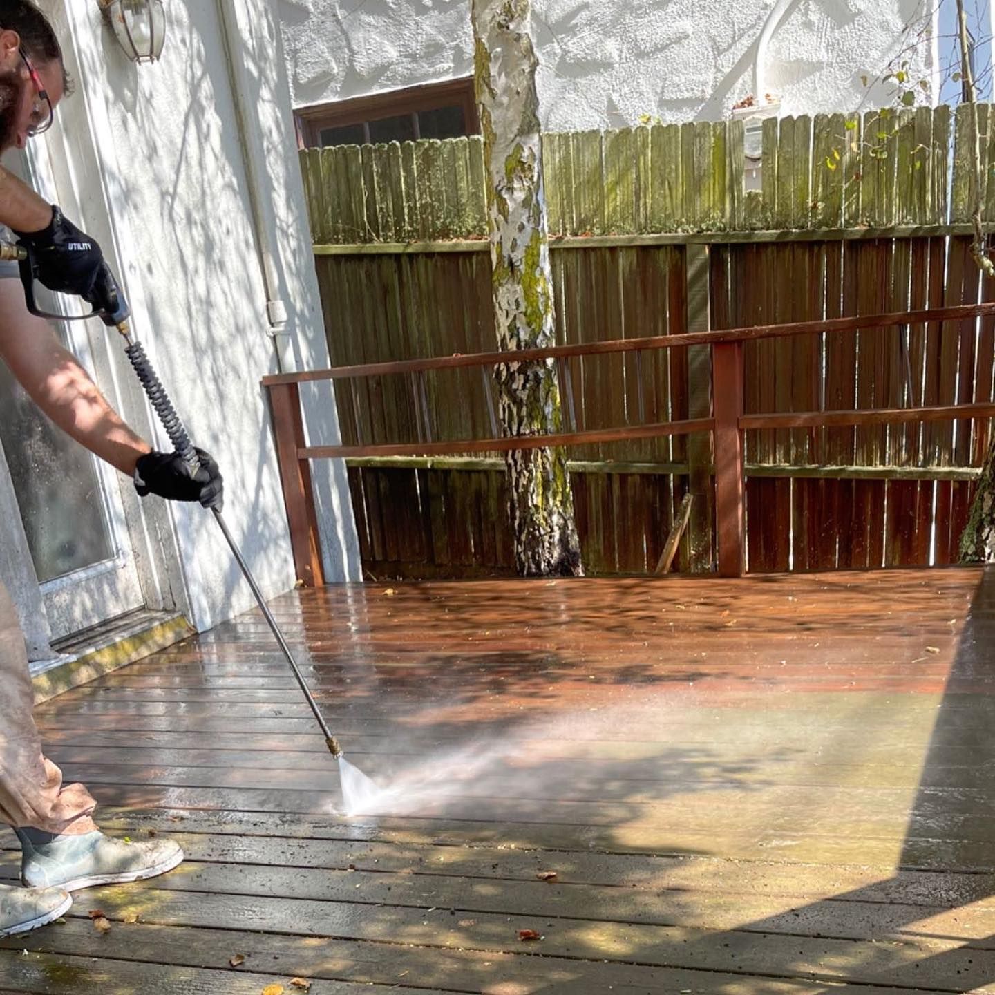 A man is using a high pressure washer to clean a wooden deck.