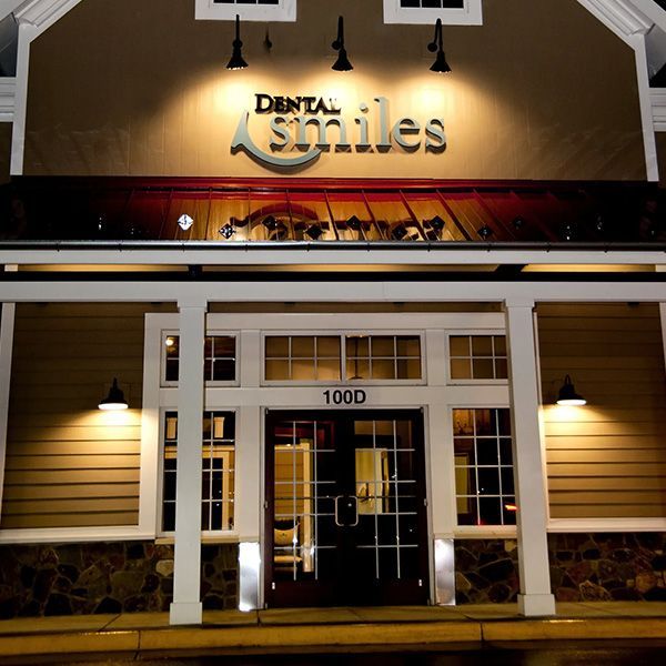 Illuminated storefront for a dental office at night, with white columns and the sign “Denta Smiles.”