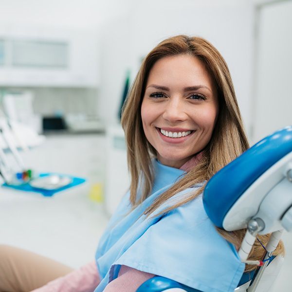 Smiling woman in a dental chair wearing a blue bib in a bright clinic