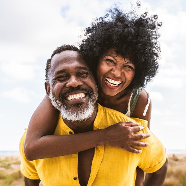 Smiling couple at the beach, one giving the other a piggyback ride