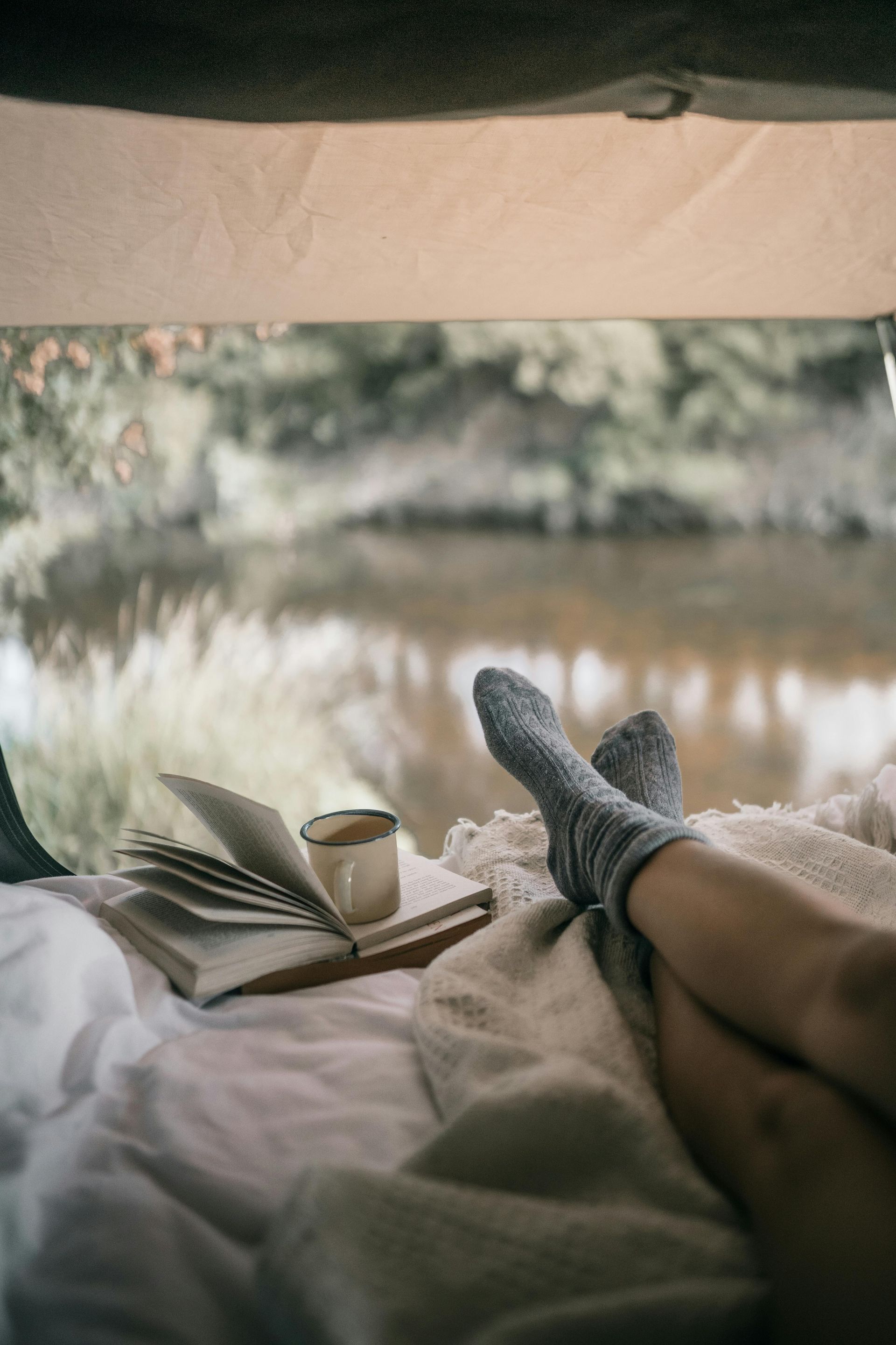 A person is laying on a bed with a book and a cup of coffee.