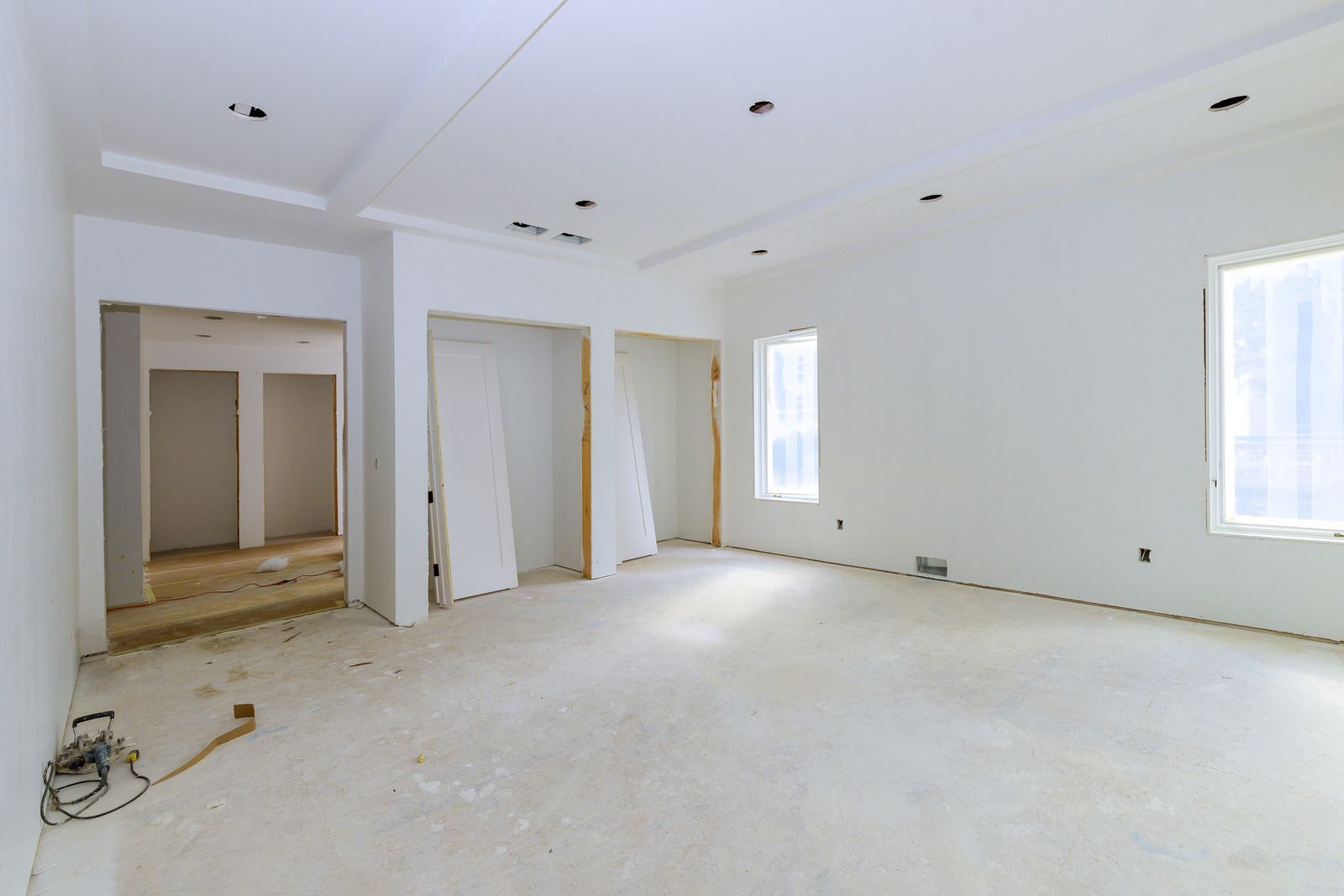 Empty interior room with white walls, unfinished doorways, and a concrete floor.