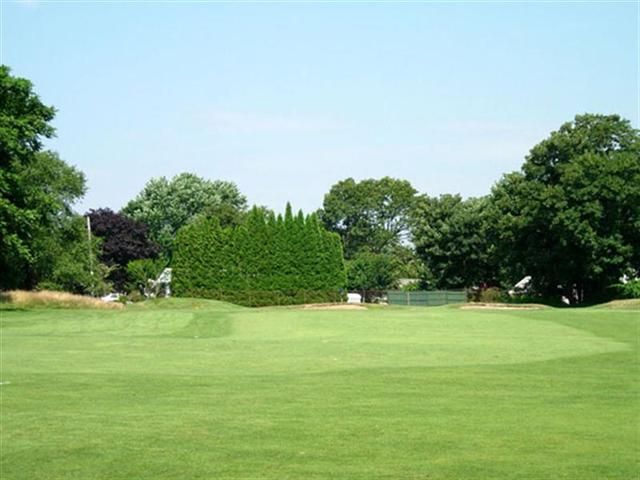 Wide green lawn bordered by trees under a clear blue sky