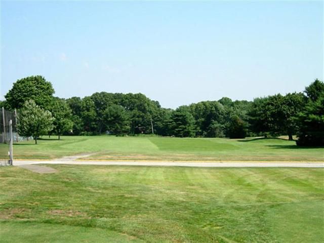 Grassy golf course fairway with sand bunker, trees, and blue sky