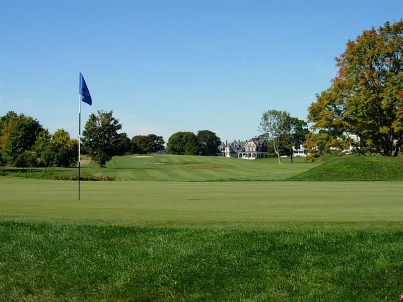 Golf course green with a flagstick under a clear blue sky