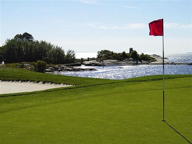 Golf green beside water with a red flag and sandy bunkers on a sunny day
