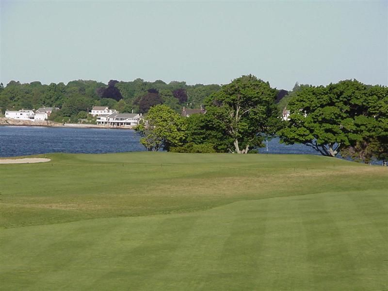 Golf course beside blue water and houses on a tree-lined shore