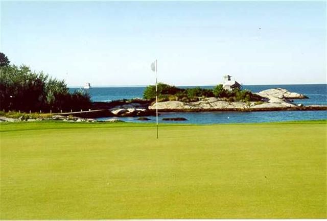 Golf green by the ocean with a flagstick and small rocky island in the background