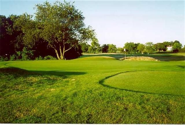 Green golf course with trees, sand bunkers, and a fairway under a clear sky