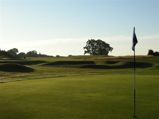 Golf green with a flagstick at sunset, rolling hills and trees in the background