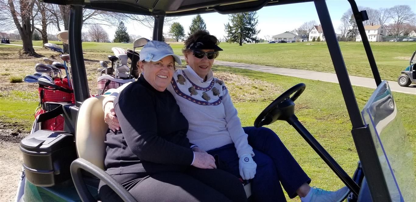 Two people sitting in a golf cart, smiling outdoors on a sunny day.
