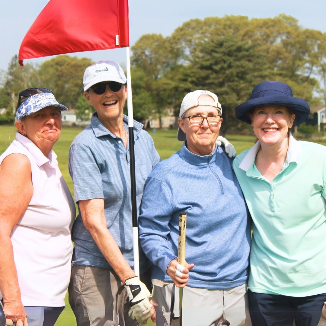 Four smiling golfers posing by a red flag on a sunny green