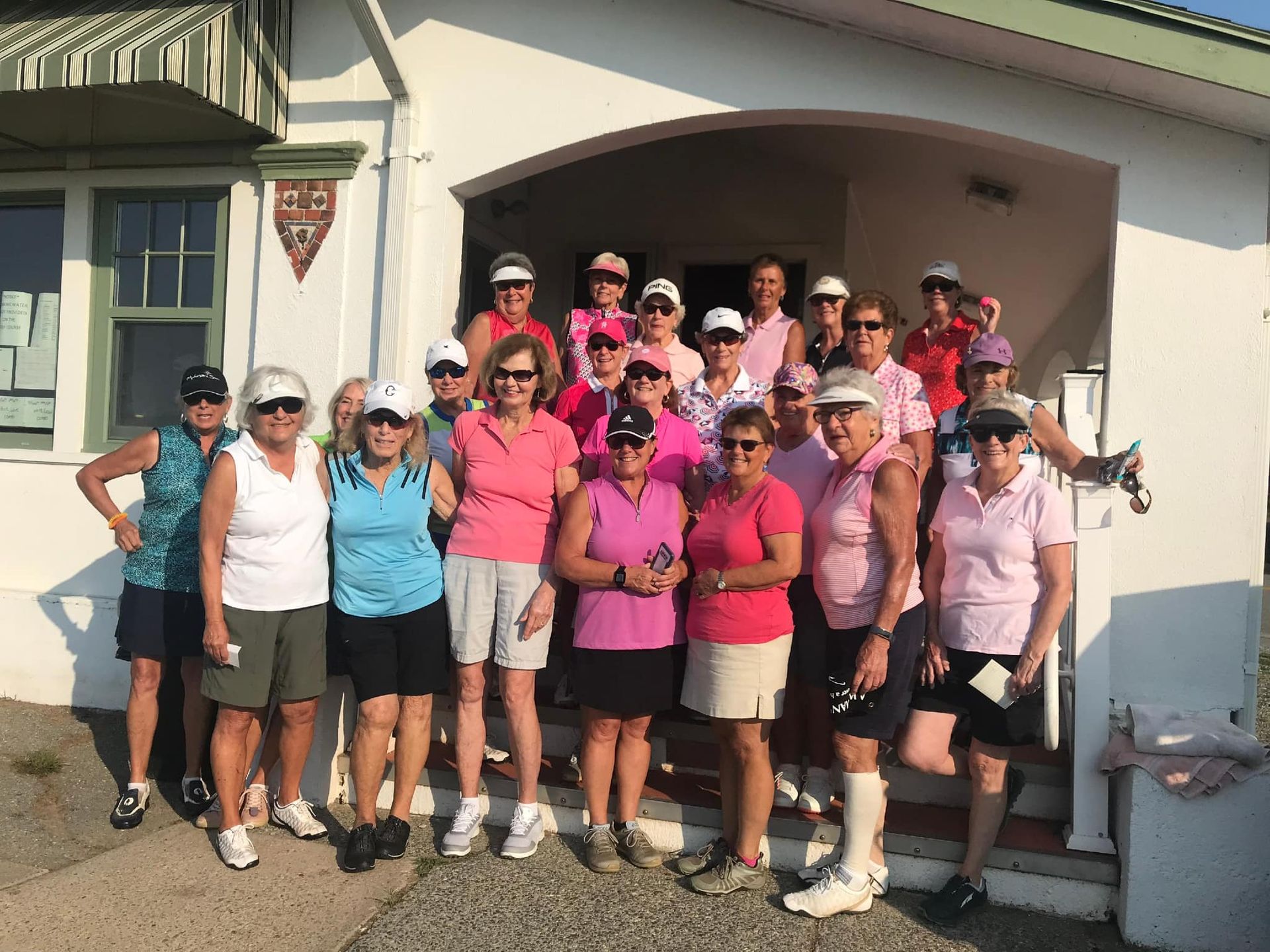 Group of cyclists in pink and blue shirts posing outside a building in bright sunlight