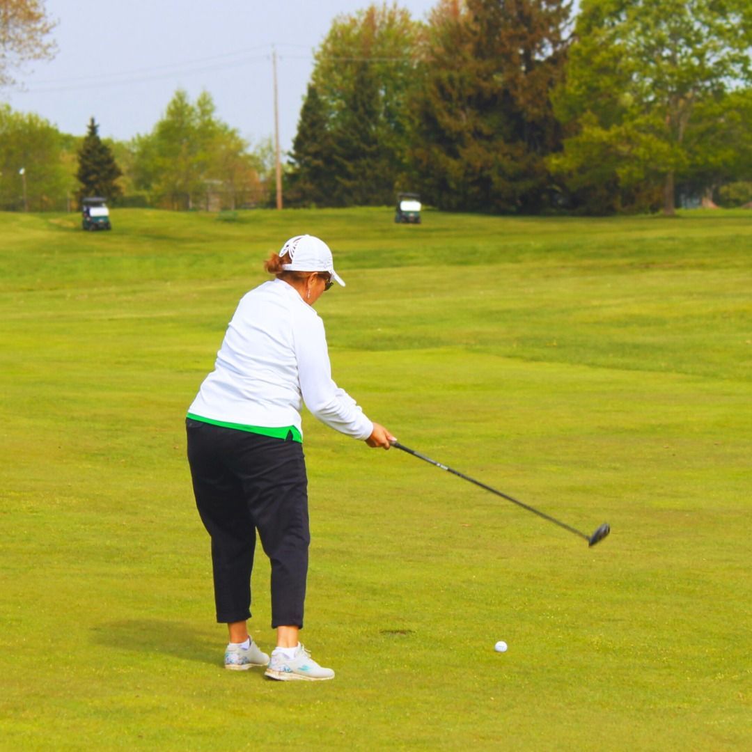 Golfer in white shirt and cap prepares to hit a ball on a green fairway under overcast skies