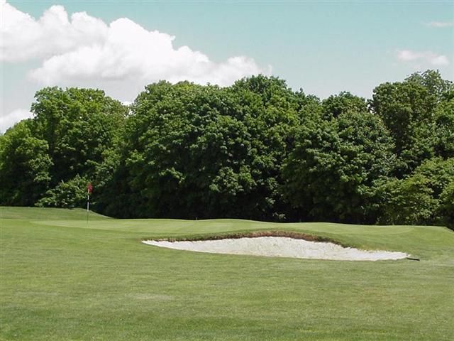Golf course fairway with a sand bunker and trees under a partly cloudy sky