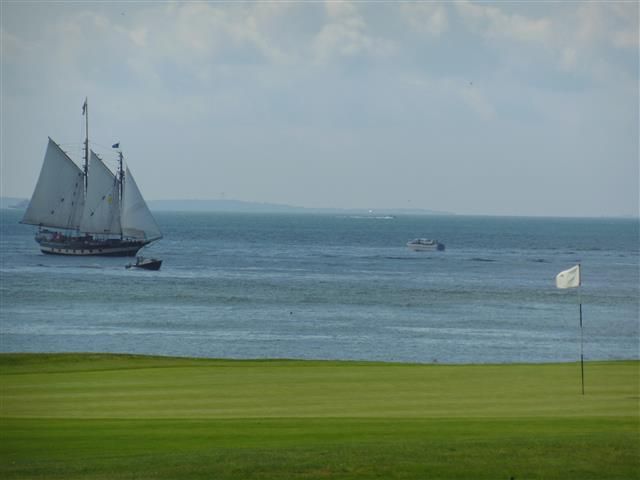 Sailboat on calm blue water beside a green shoreline under a cloudy sky