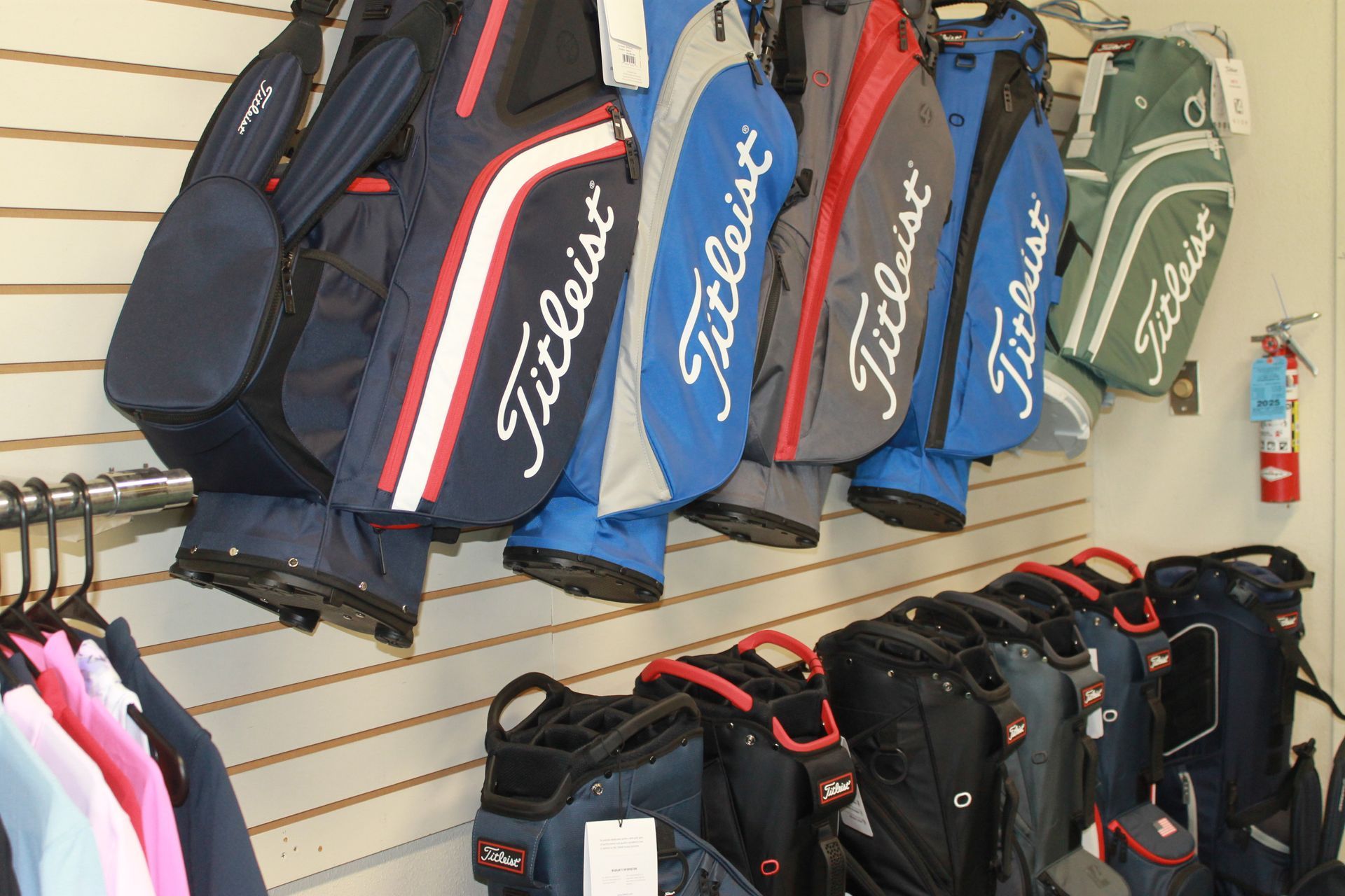 Golf bags displayed on a store wall in navy, black, blue, and green with Titleist branding