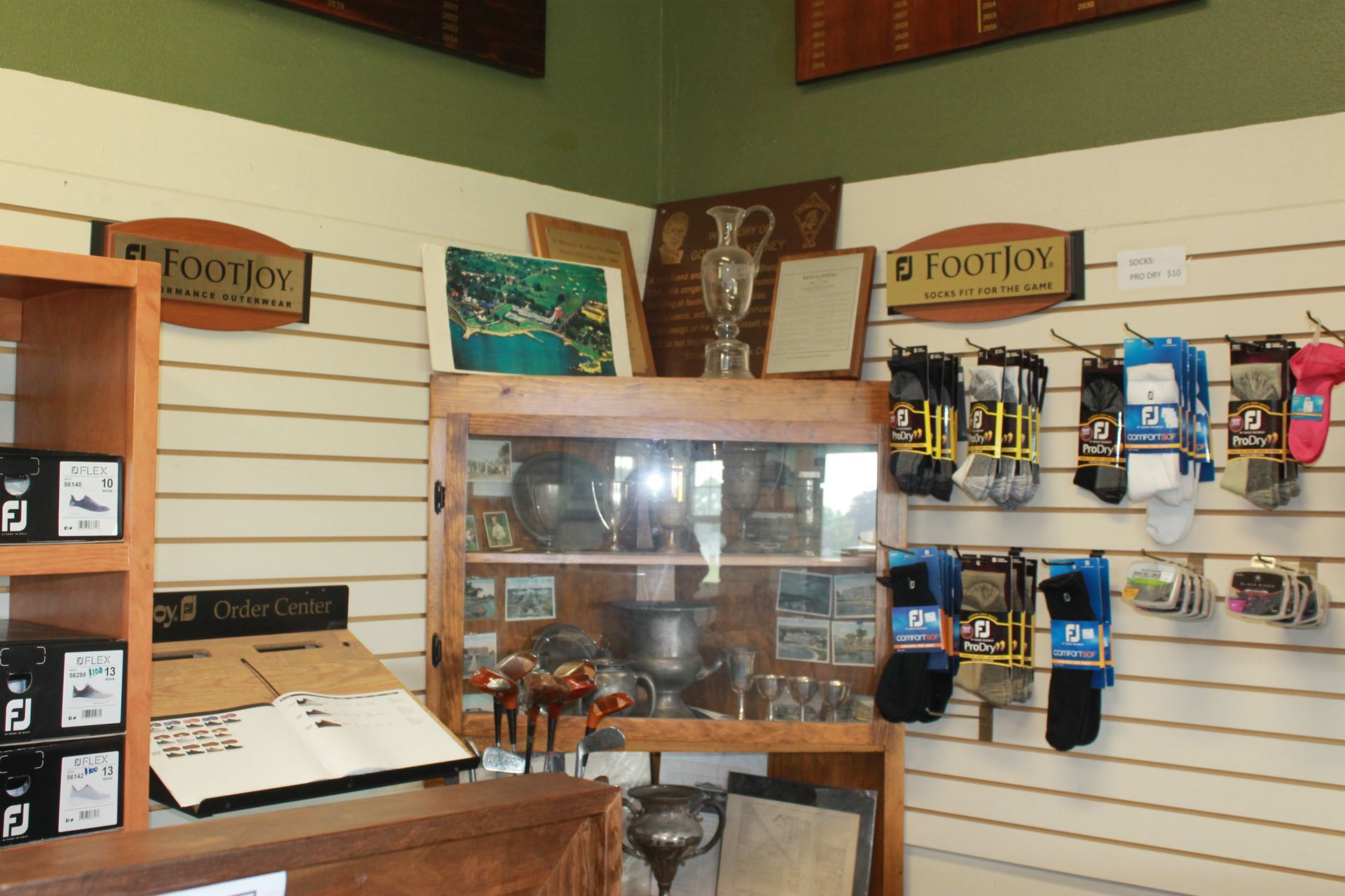 Small retail shop interior with display shelves, hanging products, and a wooden counter under a slatted wall.