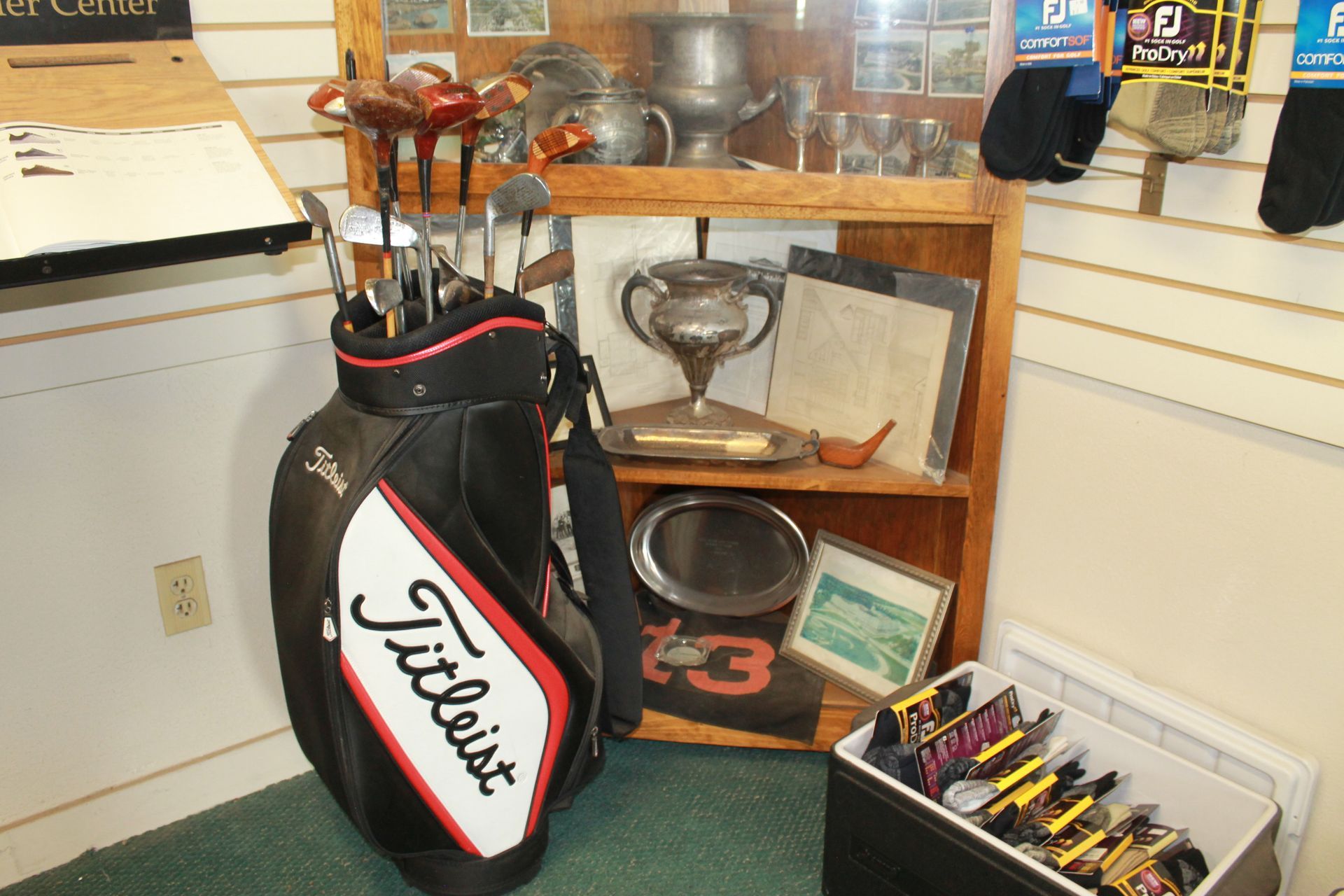 Display of golf memorabilia with a Titleist golf bag and trophies on shelves