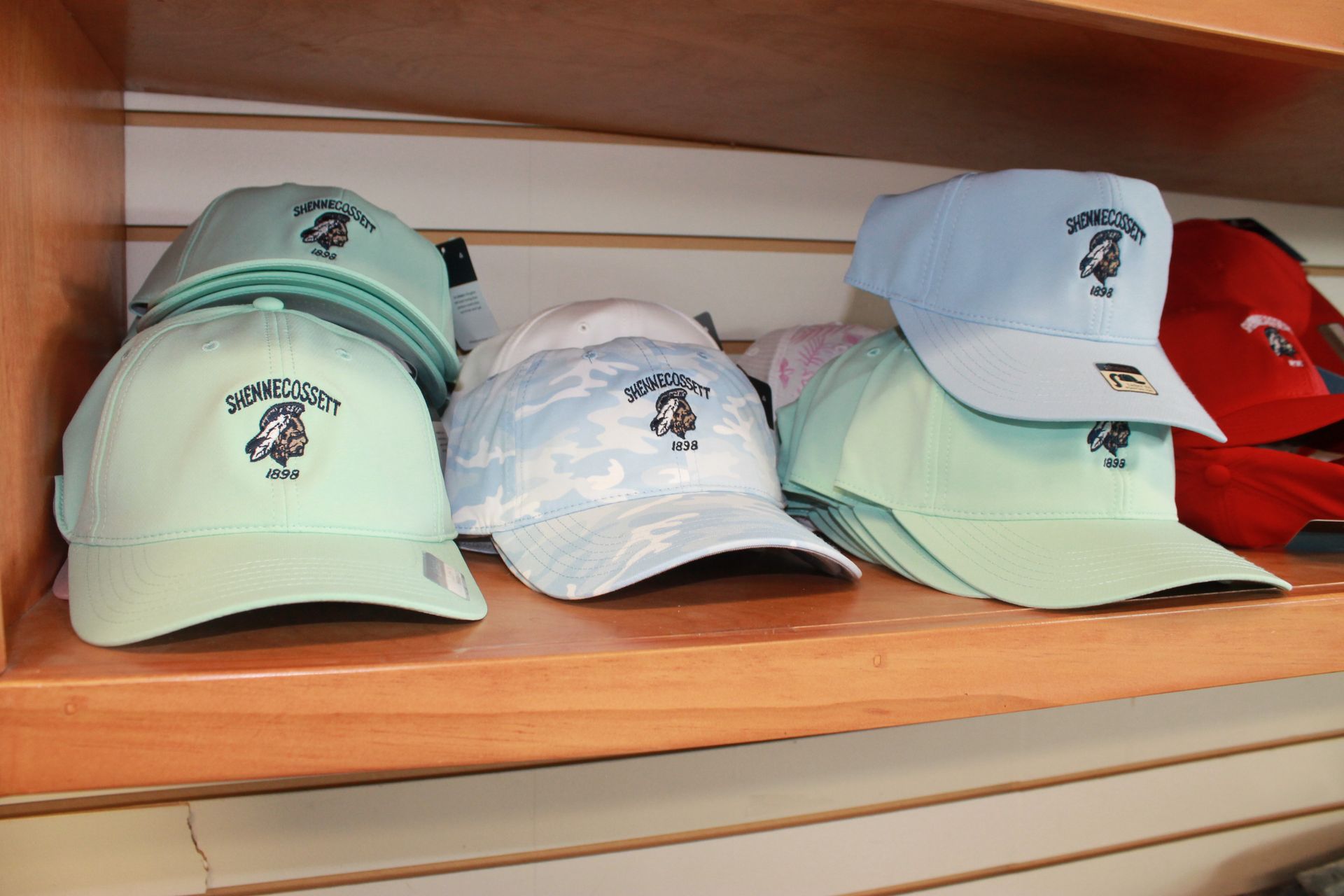 Piled baseball caps in mint green, white, and red on wooden shelves