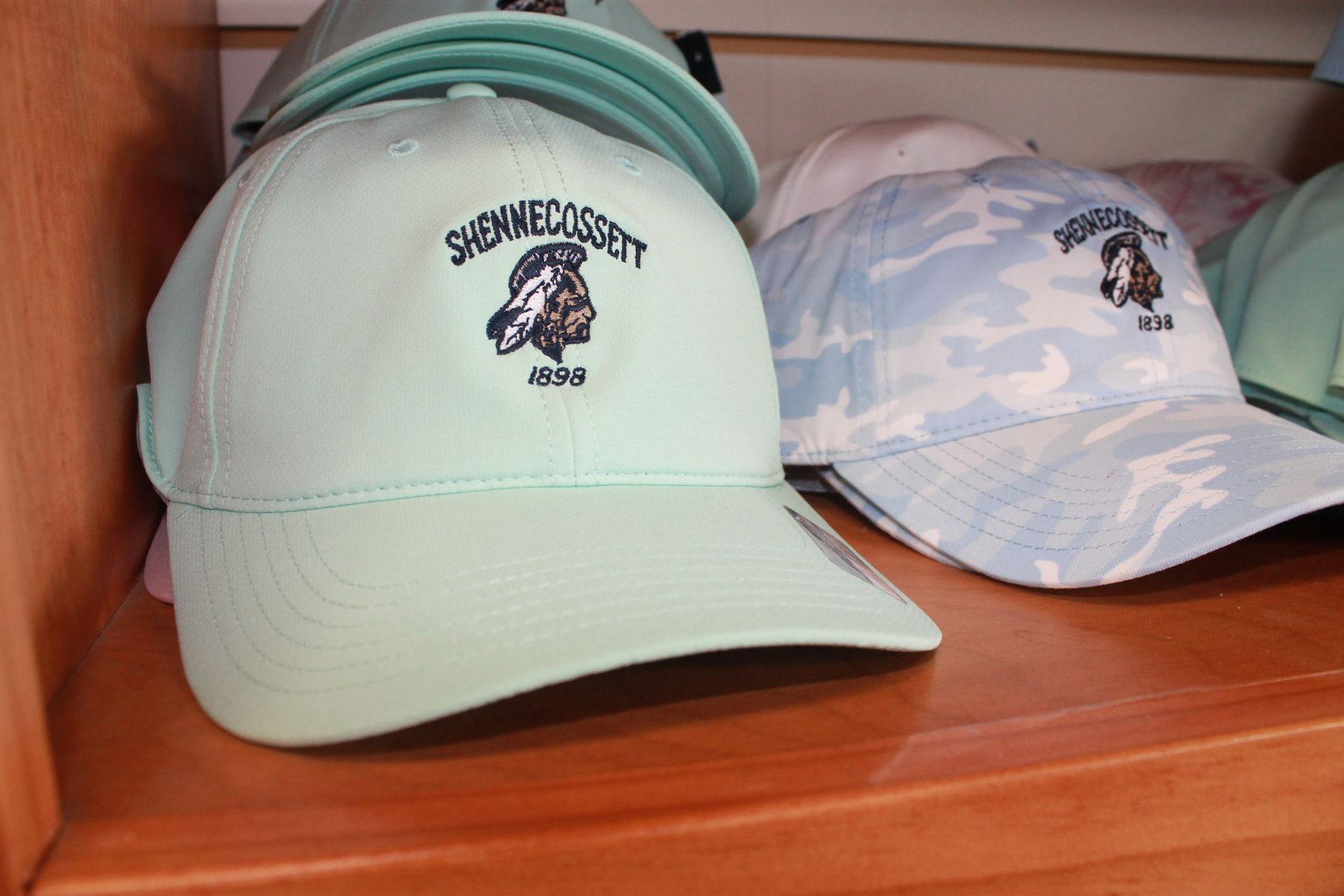 Two mint and light blue baseball caps with logos displayed on a wooden shelf
