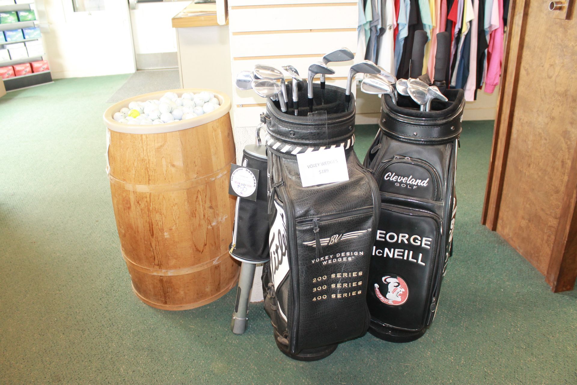 Golf bags on a store floor next to a wooden barrel display