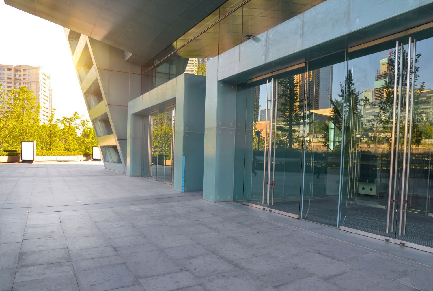 Modern glass building entrance with reflective windows and a sunlit concrete plaza