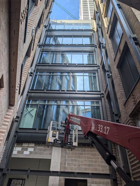 Narrow alley with a glass-fronted building and a red crane lifting materials near the entrance