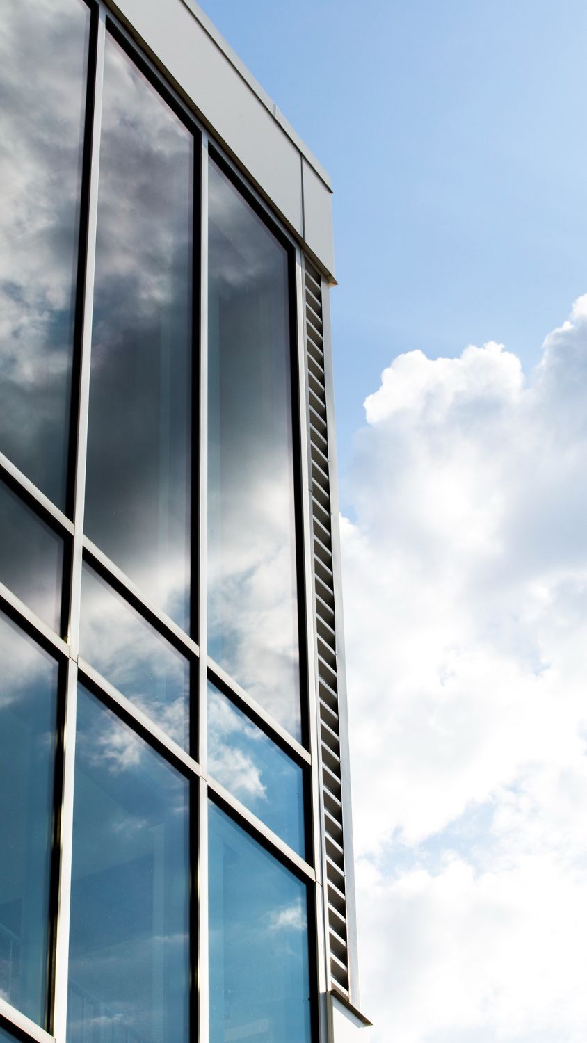 Glass office building corner against a blue sky with white clouds