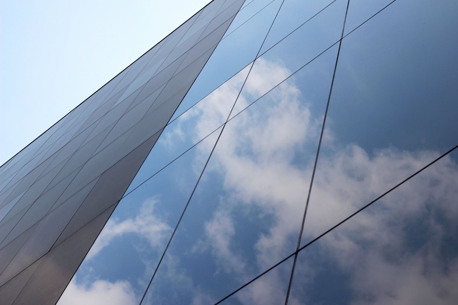 Modern glass building facade reflecting blue sky and clouds