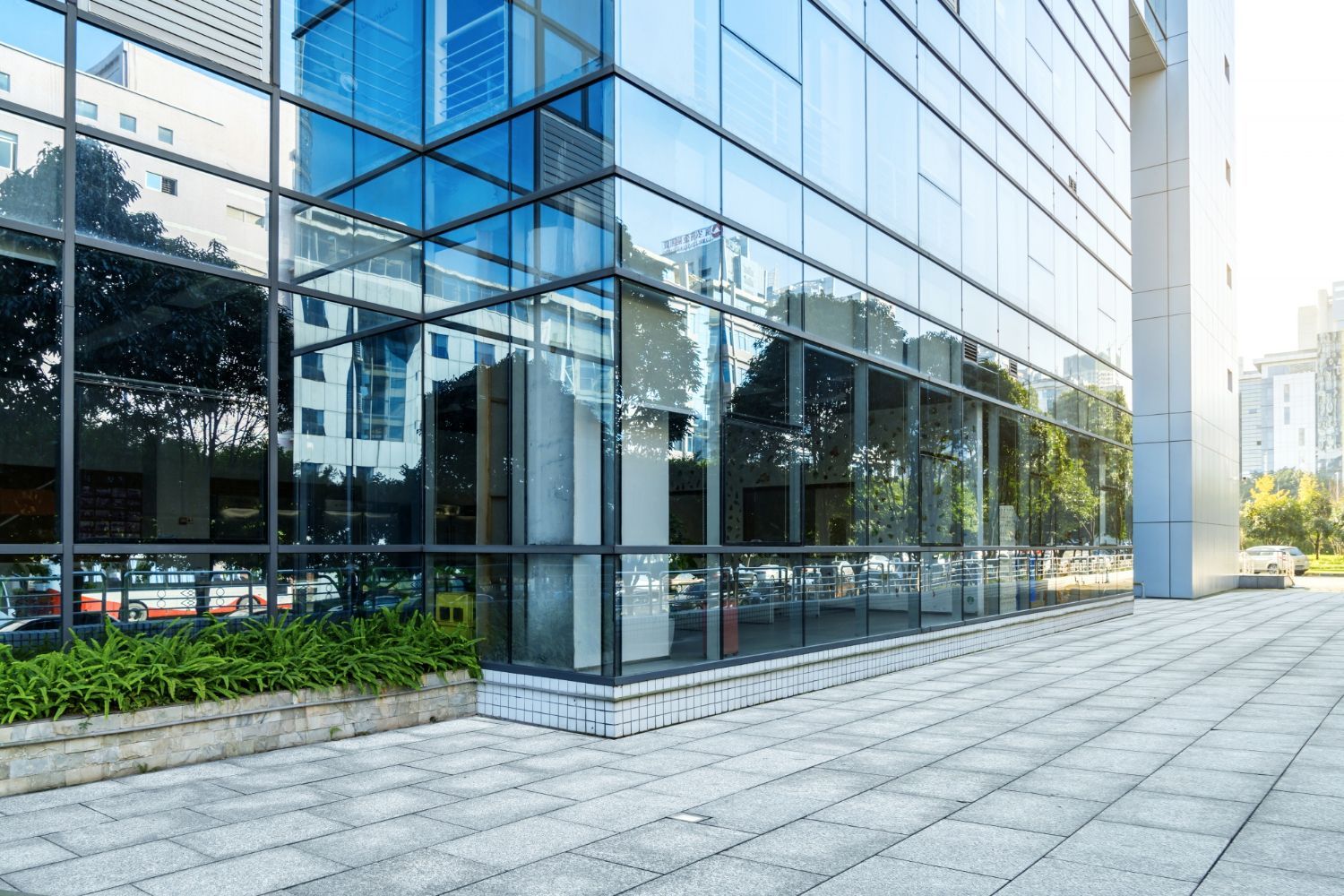 Modern glass office building with reflective windows and a wide paved sidewalk in front