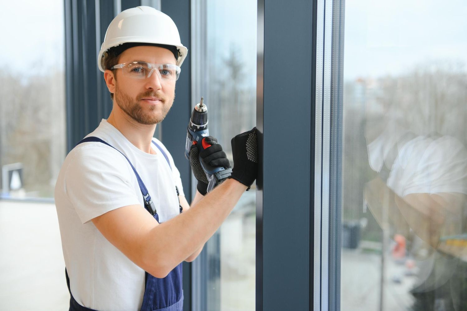 Worker in hard hat and gloves installing a window frame indoors.