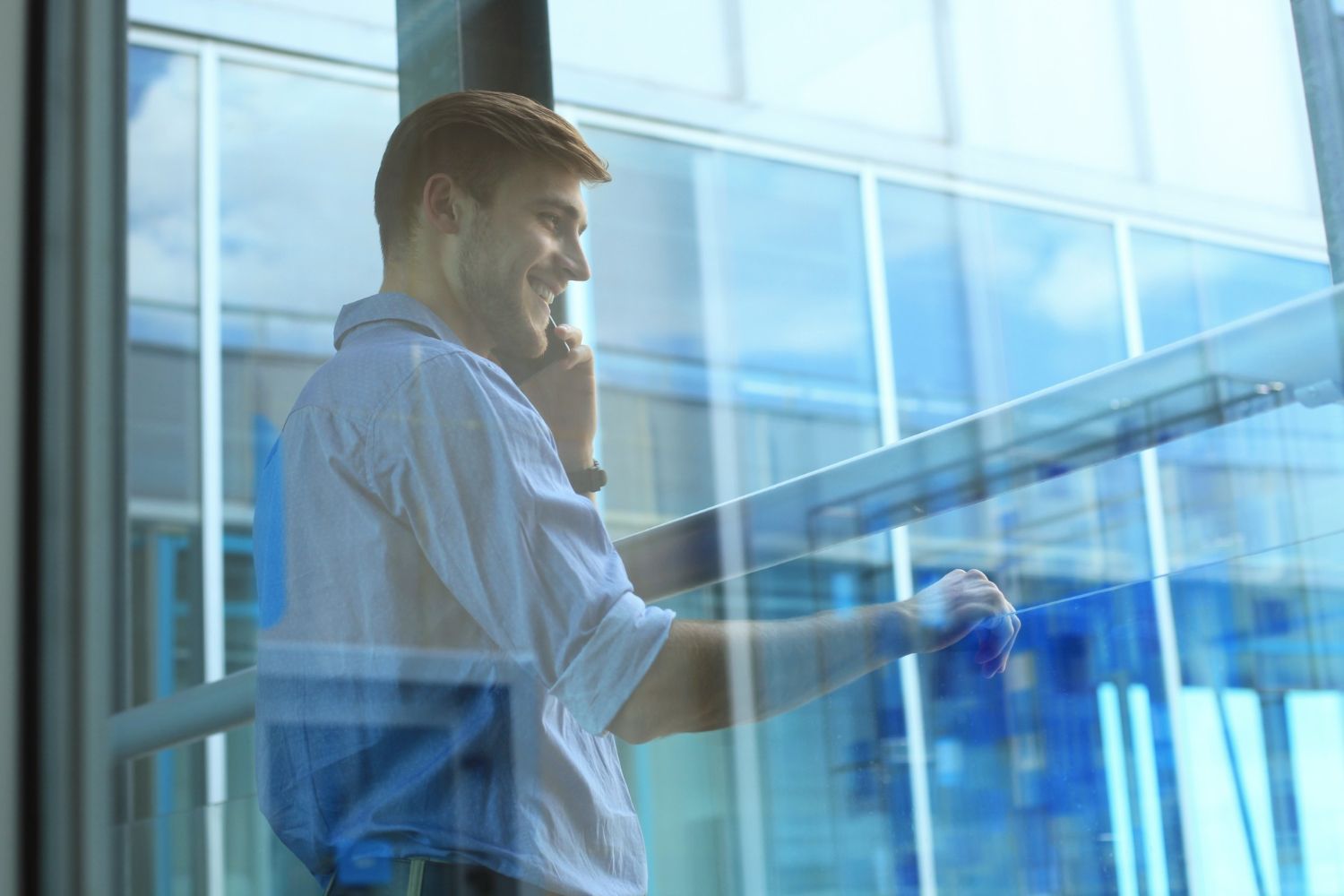 Man in blue shirt talking on a phone behind a glass wall, with sunlight streaming in