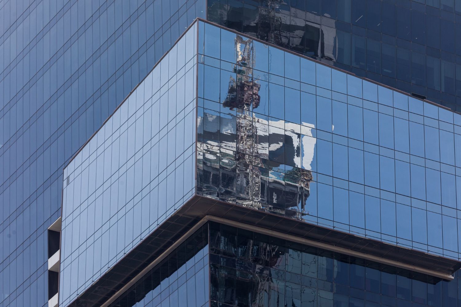 Glass-clad office building corner reflecting nearby tower and sky