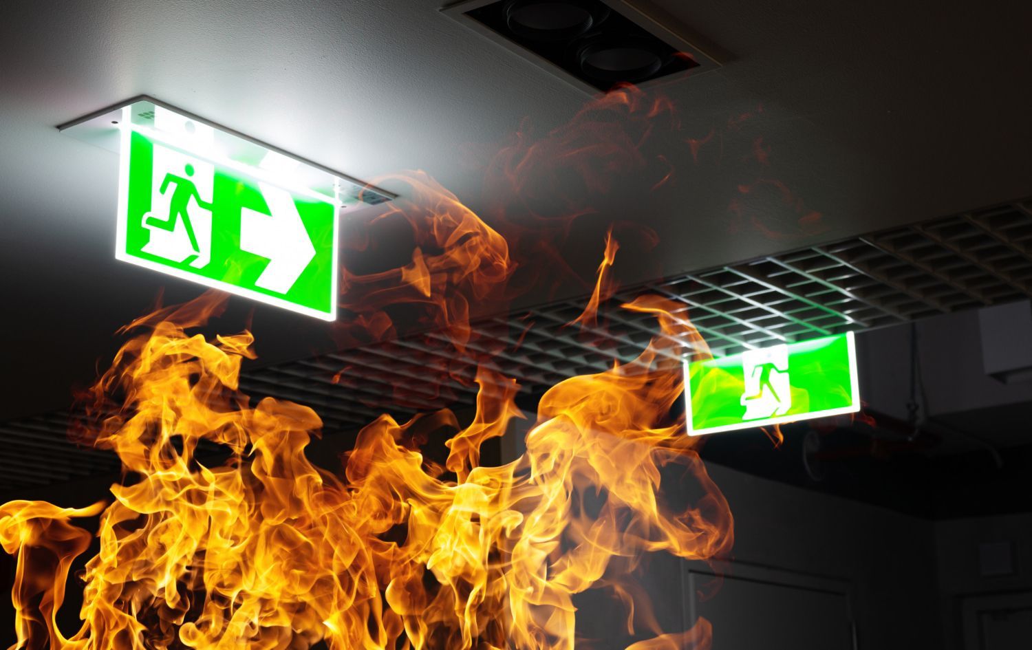 Ceiling fire under glowing green exit signs in a dark corridor