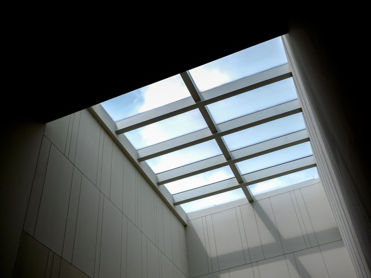 Skylight ceiling over a white atrium, with blue sky visible through glass panels.
