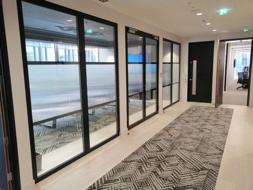 Modern office hallway with glass walls, patterned carpet, and recessed lighting