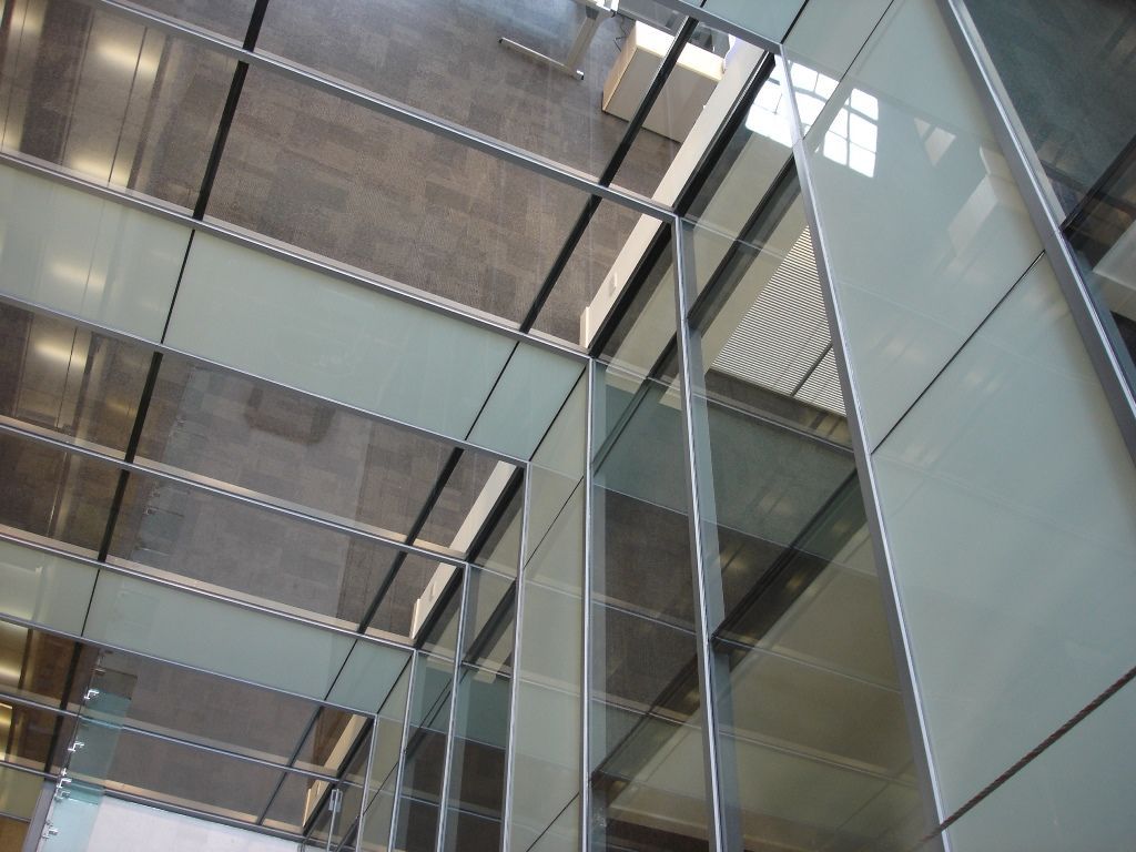 Modern glass building facade with reflective panels and steel beams, viewed from below