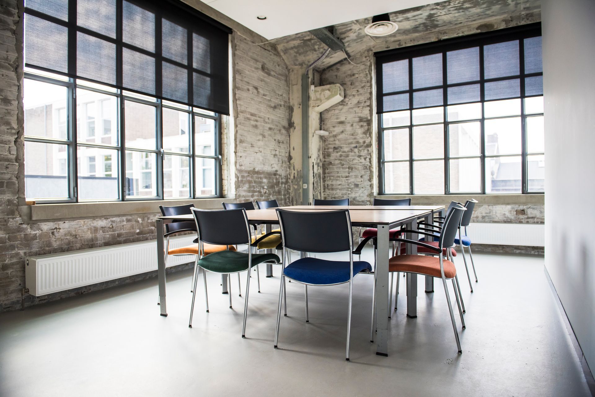 Bright modern meeting room with large windows, a long table, and assorted chairs on a concrete floor