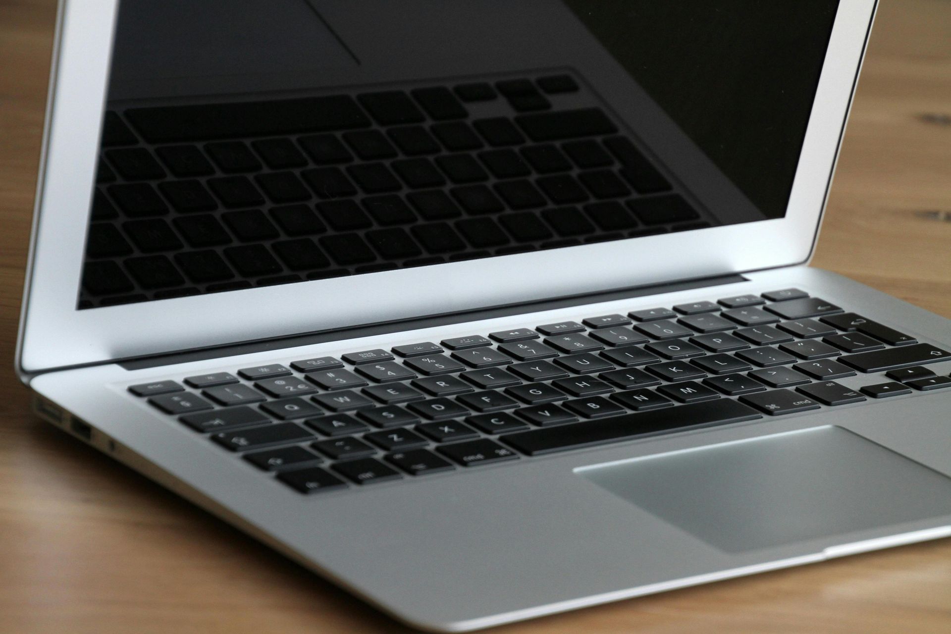Silver laptop on a wooden desk with a black keyboard and screen reflection