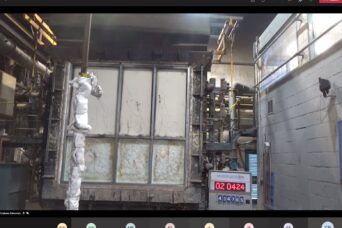 Industrial chamber with a robotic arm, foil-wrapped equipment, and a digital display in a metal room
