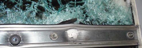 Broken car windshield with shattered glass and a damaged metal window frame.