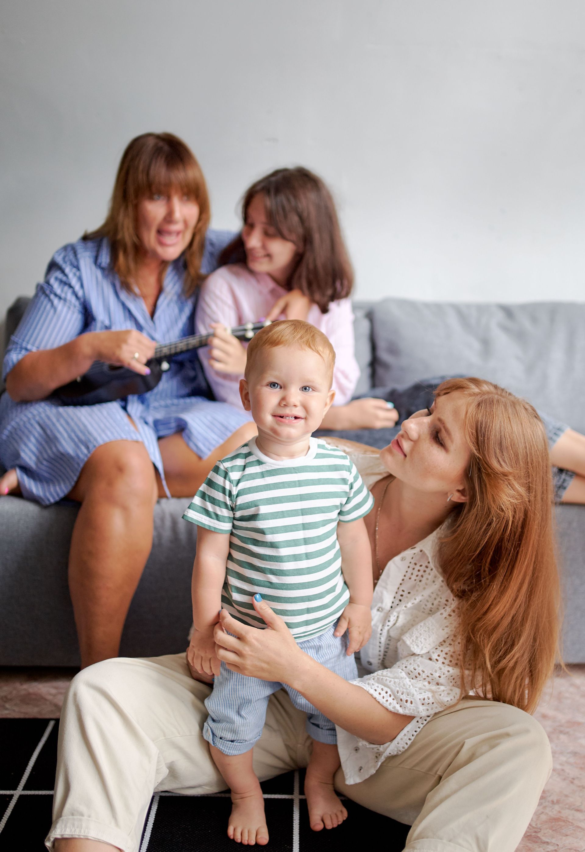 Family sitting on a couch and floor, smiling and relaxing together in a living room.