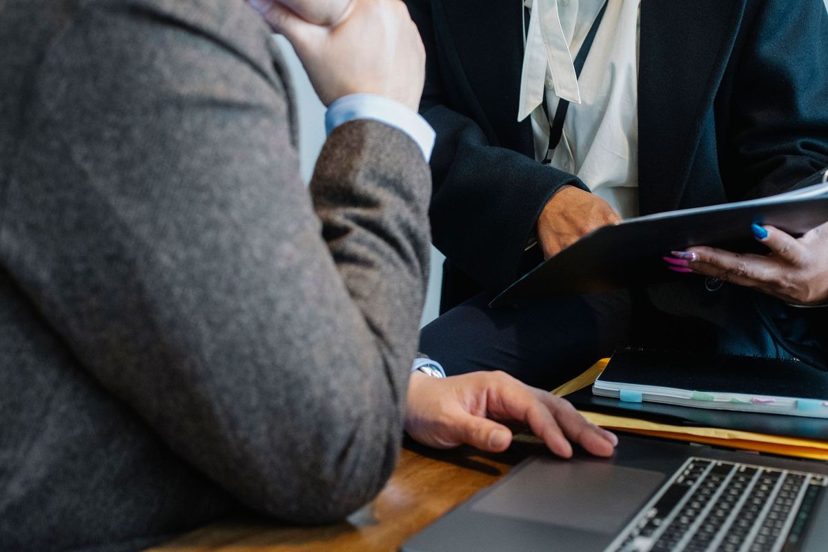 People in business attire reviewing documents and a laptop at a table.