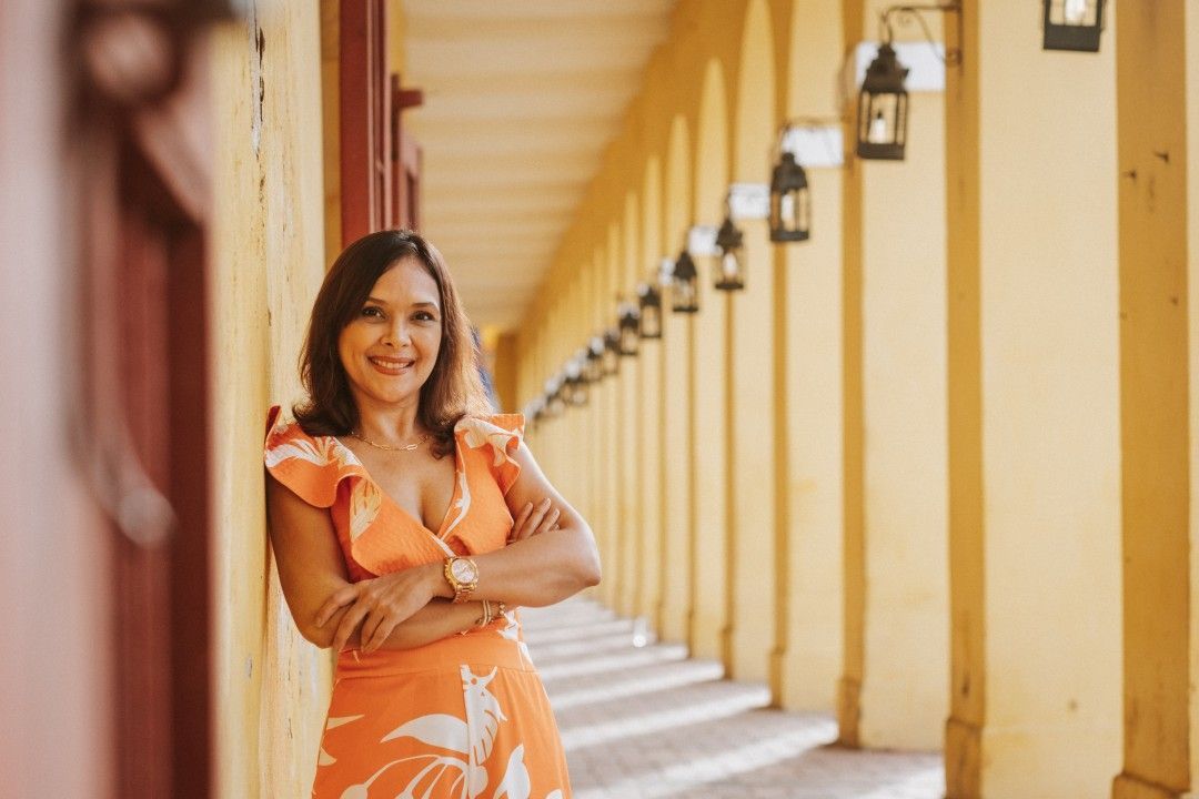 Una mujer con un vestido naranja está apoyada contra una pared con los brazos cruzados.