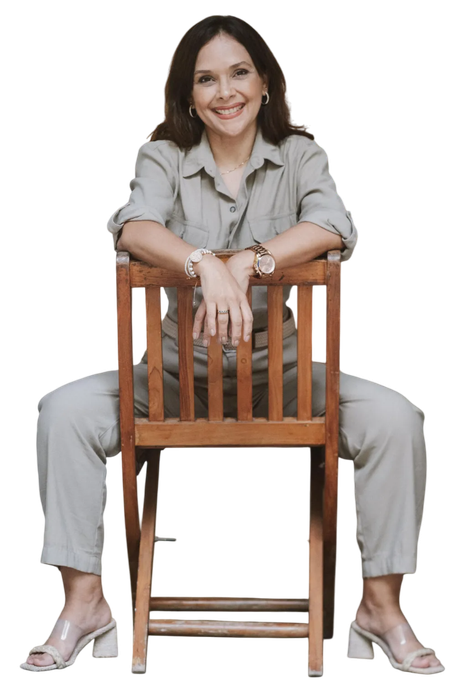 Una mujer está sentada en una silla de madera con las piernas cruzadas.
