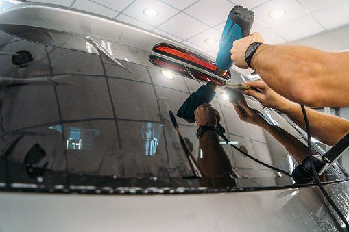 A man is polishing the rear window of a car with a machine.