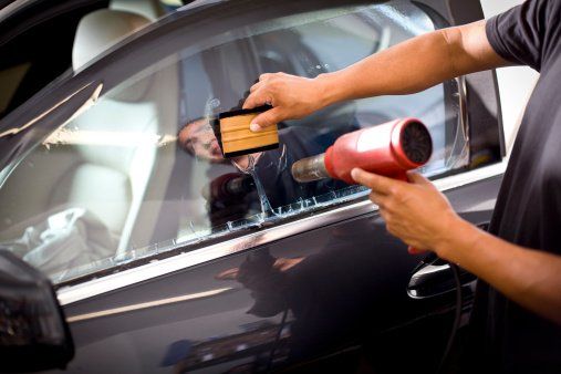 A man is applying tinted window film to a car window.